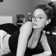 a woman laying on top of a bed in a black and white photo with glasses