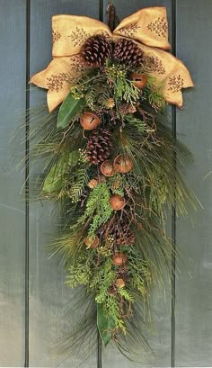 a wreath with pine cones and evergreens hanging on a blue wooden door decorated for christmas