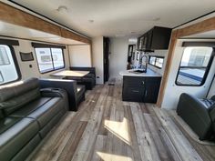 the interior of an rv with wood flooring and leather couches, windows, and kitchen