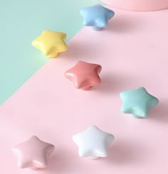 five small stars on a pastel pink and blue surface next to a white vase