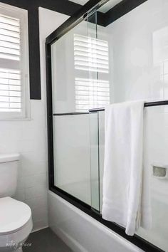 a white toilet sitting next to a bath tub under a bathroom window with blinds on it