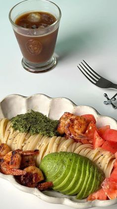 a plate with pasta, avocado and shrimp on it next to a cup of coffee