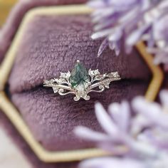 an engagement ring with a green stone surrounded by white diamonds on a purple velvet surface