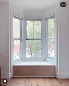 an empty window seat in the corner of a room with wood floors and white walls