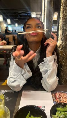 a woman sitting at a table with chopsticks in front of her mouth and vegetables on the plate