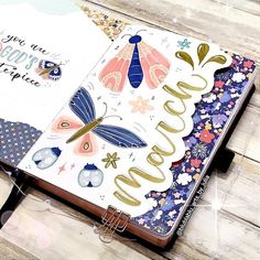 an open planner book on a wooden table with flowers and butterflies in the pages that spell out happy new year