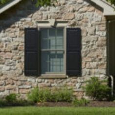 a brick house with black shutters and green grass