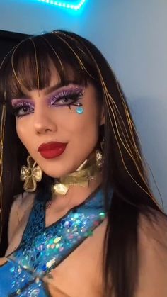 a close up of a woman with makeup and hair wearing blue dress, gold necklace and earrings