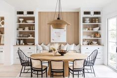 a dining room table surrounded by chairs in front of white cabinets and open shelving