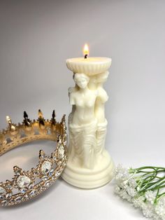 a candle that is next to a tiara on a white surface with flowers in the foreground