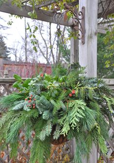 a potted plant hanging from a wooden post on a deck with greenery and berries