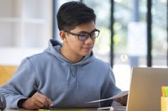 a young man sitting at a table with a laptop and pen in front of him