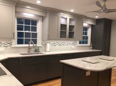 a large kitchen with marble counter tops and gray cabinets, along with a ceiling fan