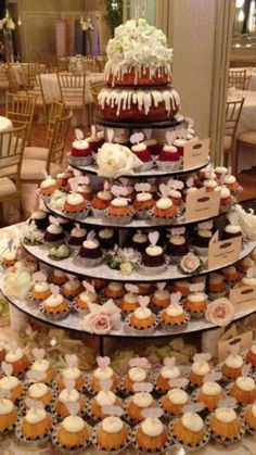 a tiered cake with cupcakes and flowers on the top is surrounded by other desserts