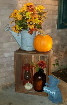 an arrangement of pumpkins, flowers and other items are displayed on a wooden crate