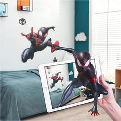 a person holding up an ipad with a spider man wall decal on it