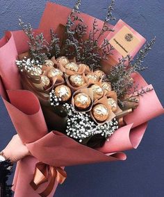 a bouquet of flowers with chocolates wrapped in pink paper and tied to a blue wall