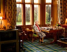 an older woman sitting at a desk in a room with large windows and plaid carpet