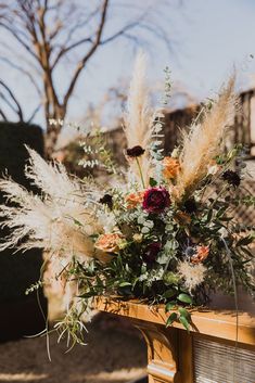 a vase filled with flowers and feathers on top of a wooden table next to a fence