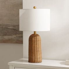 a wicker lamp on a white table next to a brown and white cabinet with drawers