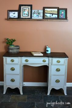 a white desk with three pictures on the wall above it and a potted plant