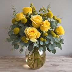 a vase filled with yellow roses and greenery