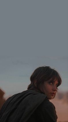 a woman standing on top of a dirt field next to a sky filled with clouds