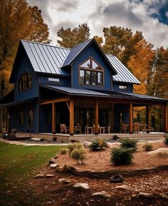 a large blue house in the woods with lots of trees and rocks on the ground