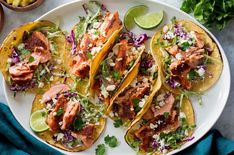 three fish tacos on a white plate with limes and cilantro sauce