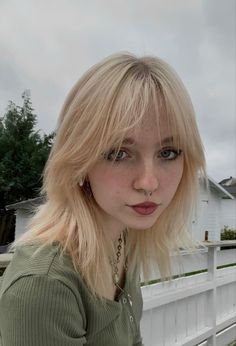 a woman with blonde hair and piercings standing in front of a white picket fence