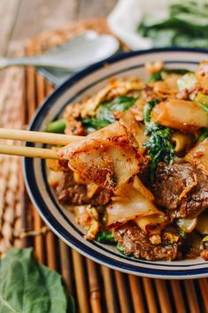 a bowl filled with meat and vegetables on top of a bamboo mat next to chopsticks