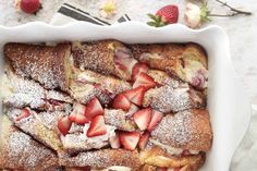 a white casserole filled with sliced strawberries and powdered sugar on top