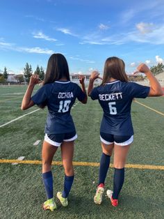 two girls in soccer uniforms are standing on the field with their hands behind their backs