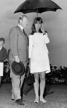 a man and woman standing under an umbrella in the grass with other people behind them