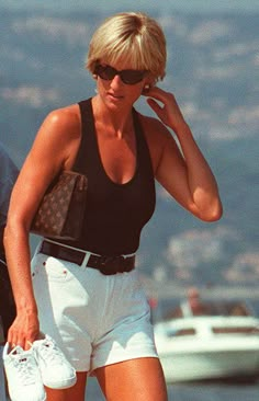 a woman in white shorts and black tank top walking on the beach with her purse