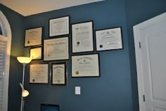 there are many framed papers on the wall next to a laptop and lamp in this room