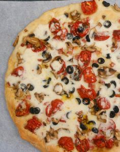 a pizza sitting on top of a table covered in cheese and toppings with olives