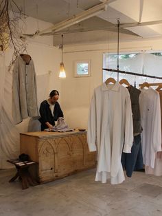 a man sitting at a table in front of some clothes on hangers and another person standing next to him