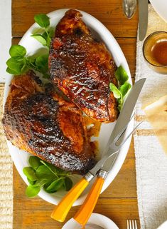 two pieces of meat sitting on top of a white plate next to a fork and knife