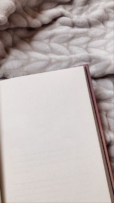 an open book sitting on top of a bed next to a white blanket and pillows