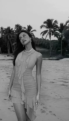 a woman standing on top of a sandy beach next to palm trees and ocean waves