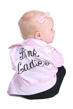 a baby sitting on the ground wearing a pink jacket and black pants with words written on it