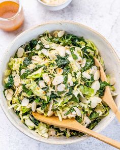 a white bowl filled with salad and wooden spoons on top of a marble counter