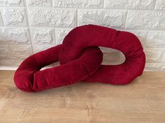 a red pillow sitting on top of a wooden floor next to a white brick wall