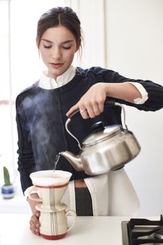 a woman pouring water into a cup on top of a counter next to a stove