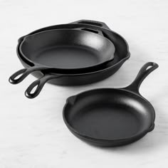 two black cast iron skillets sitting side by side on a marble countertop, one is empty