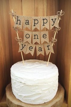 a white cake sitting on top of a wooden table next to a sign that says happy one year