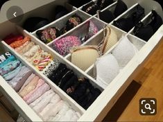 an organized drawer with clothes and bras in the bottom section, on top of a wooden floor