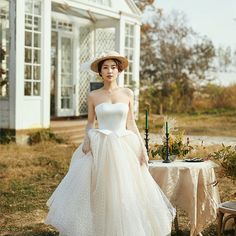 a woman in a white dress and hat standing next to a table