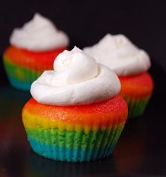 three rainbow cupcakes with white frosting on top